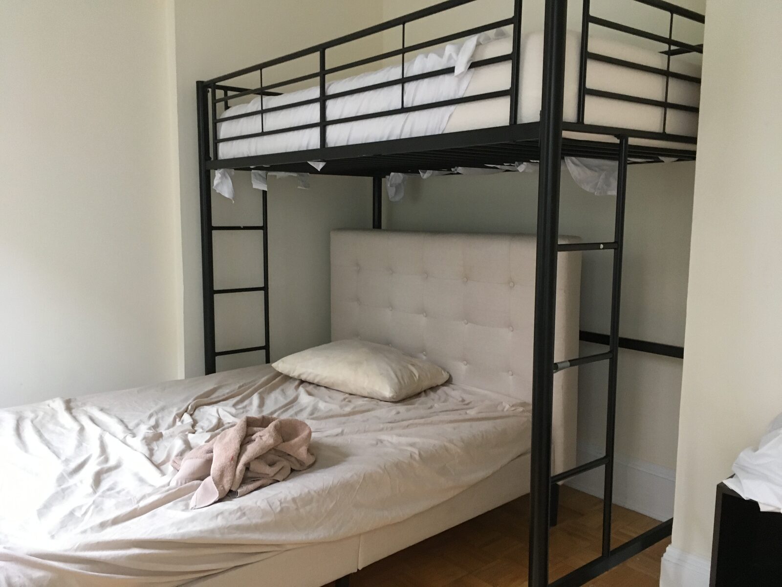 A metal bunk bed frame in a small bare room, the lower bunk unmade