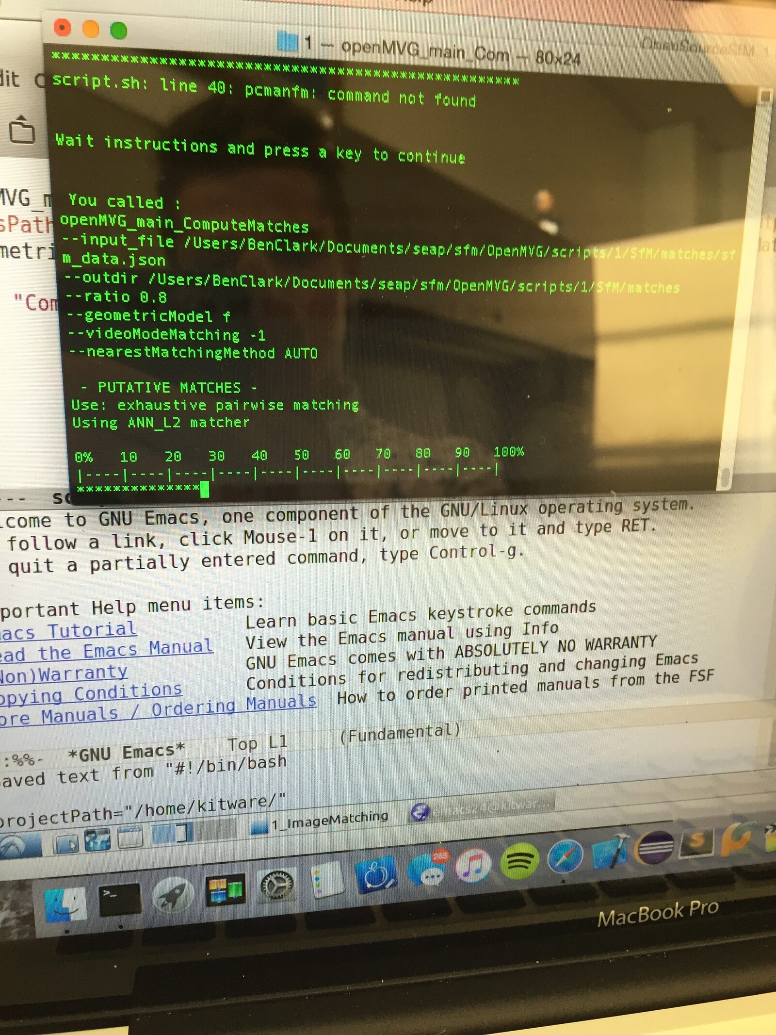 A photo of a MacBook screen running openMVG_main_ComputeMatches in a terminal, with the GNU Emacs manual open behind it