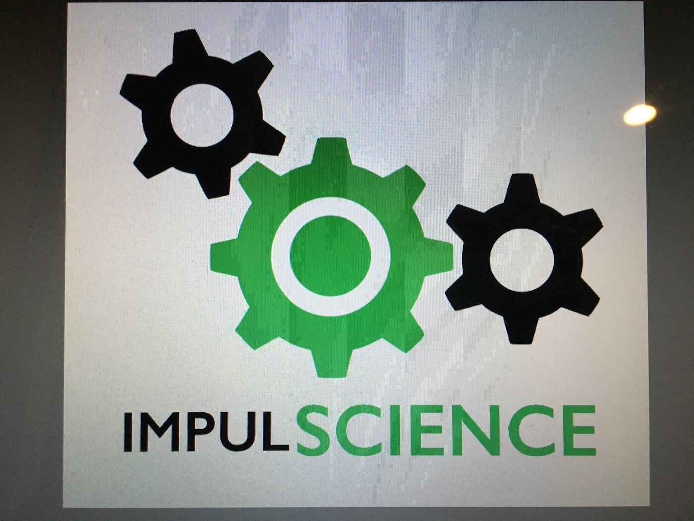A hand-painted ImpulScience sign with three interlocking gears, photographed on a wall